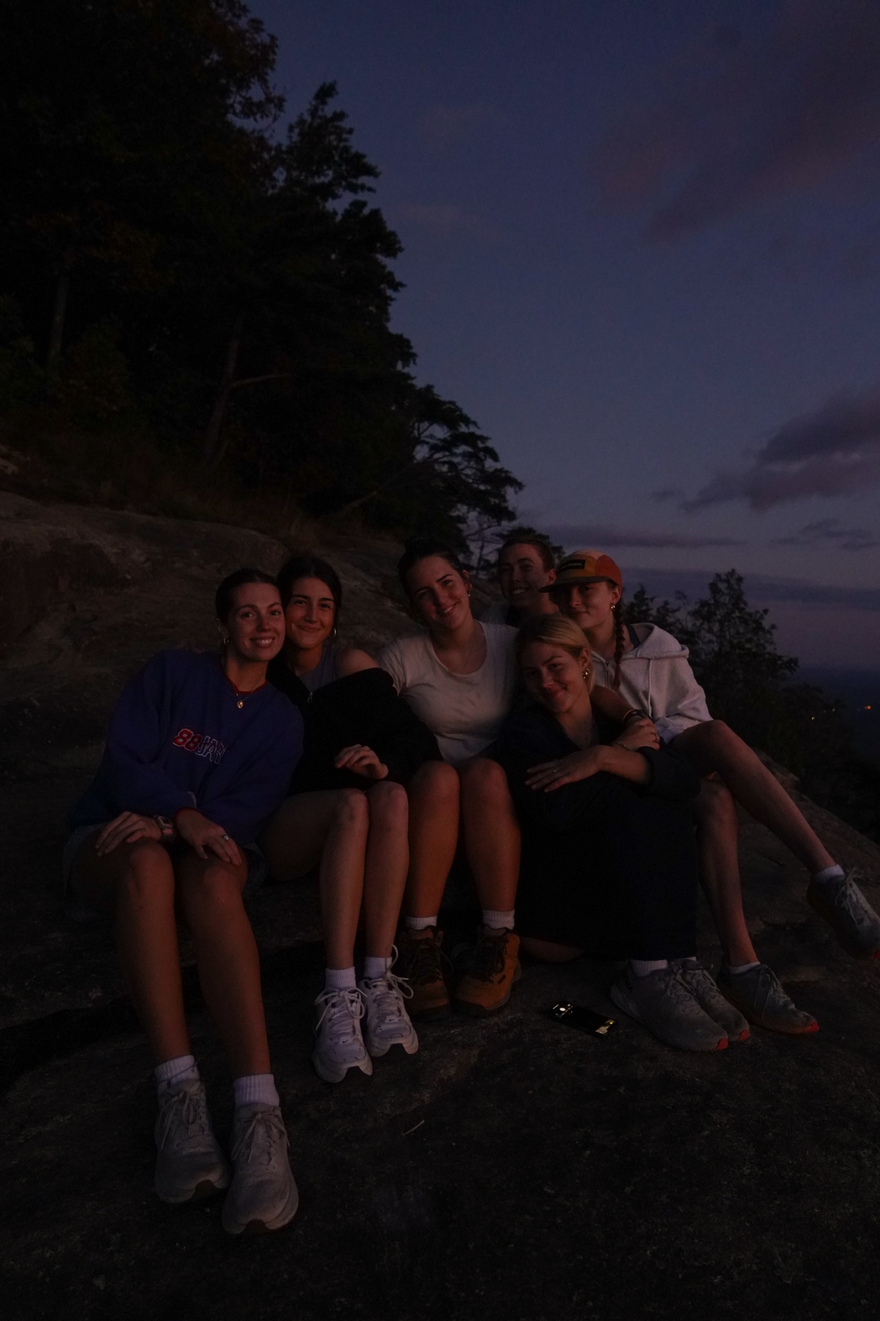 A small group of friends sitting on a rock at dusk