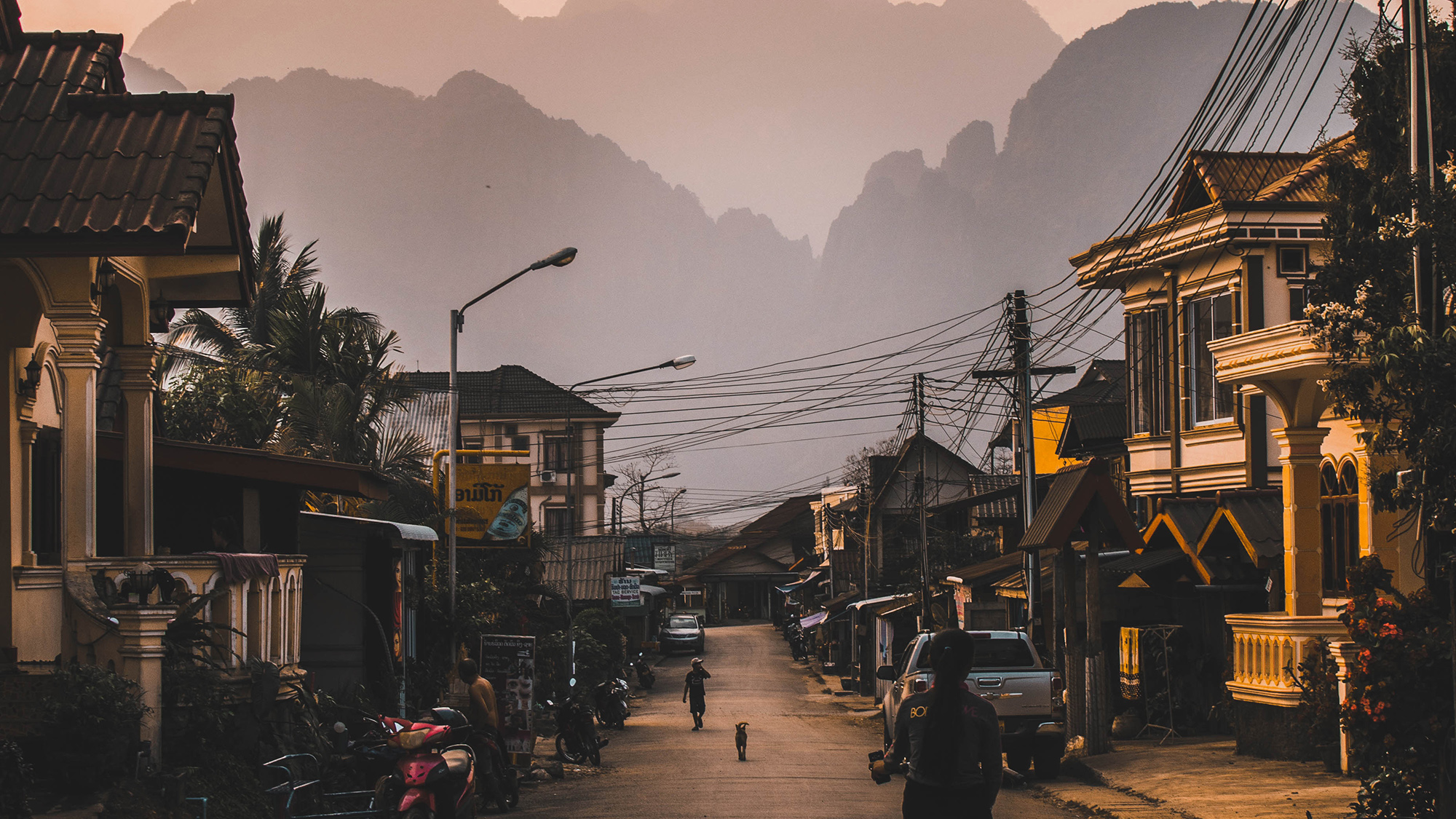 Quiet Laotian street at dusk with limestone mountains in the distance