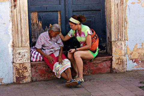 World Race participant sitting and praying with an elderly woman in a doorway