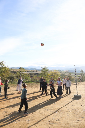 Racers and Albanian youth playing volleyball on a mountainside field at golden hour