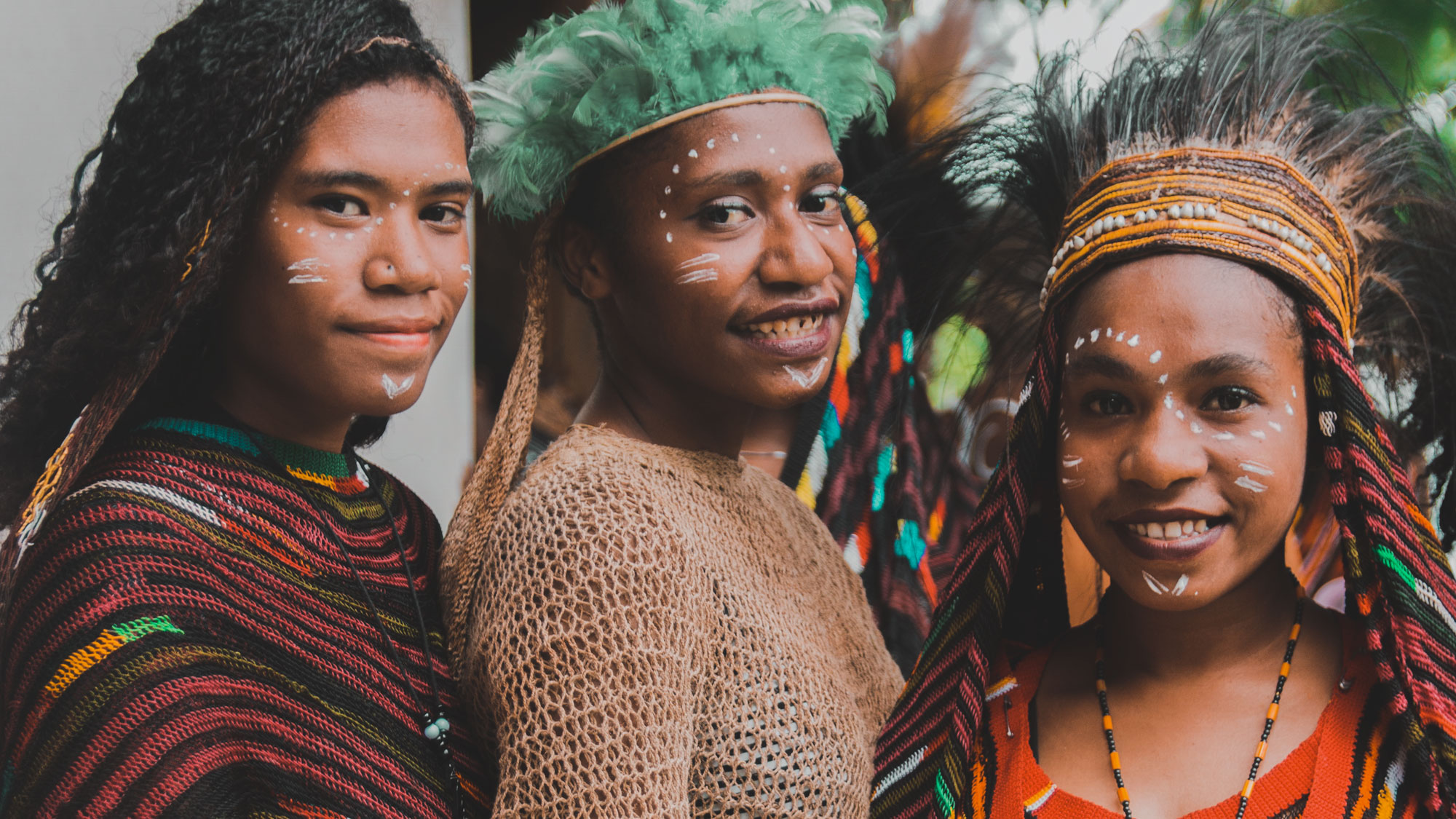 Three Papua New Guinean women in traditional dress with face paint and feathered headpieces