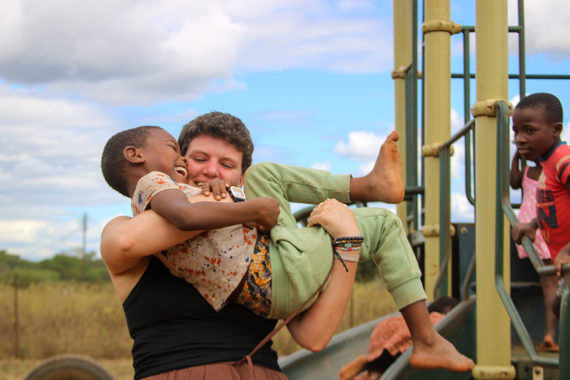 Racer laughing while lifting a South African child on a township playground